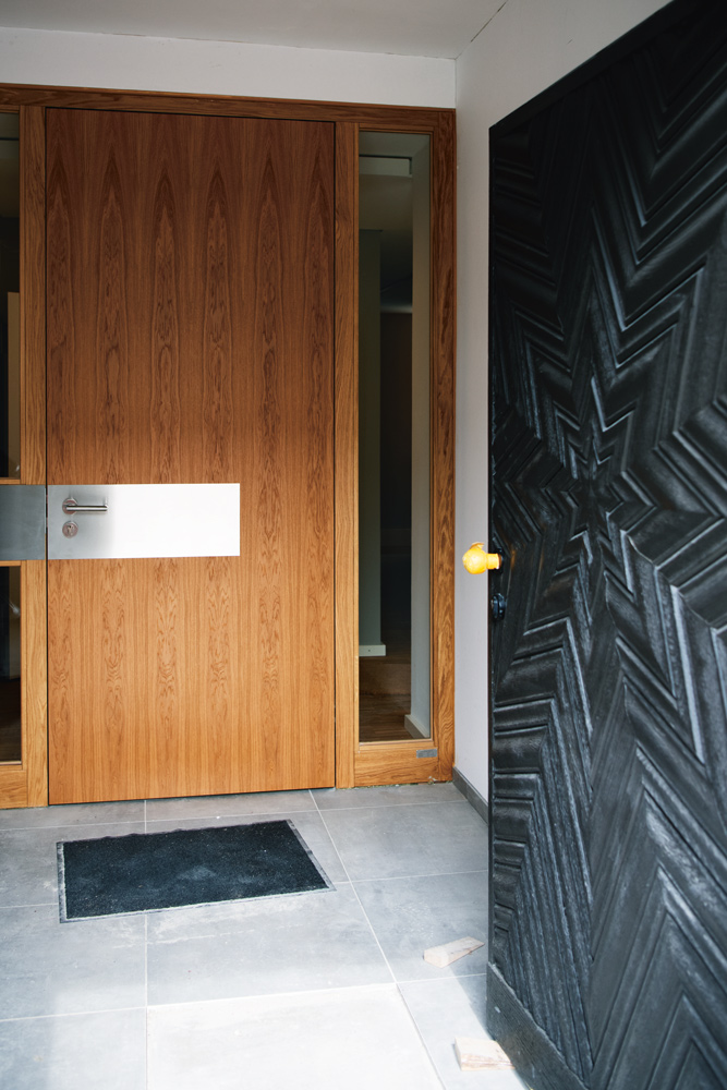 Eine geöffnete dunkle Holztür öffnet den Blick auf eine weitere, modernere Tür aus hellem Holz.