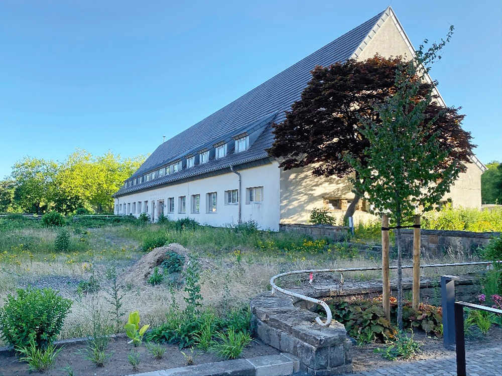Ein Bestandsgebäude mit Putzfassade und Satteldach in grüner Umgebung
