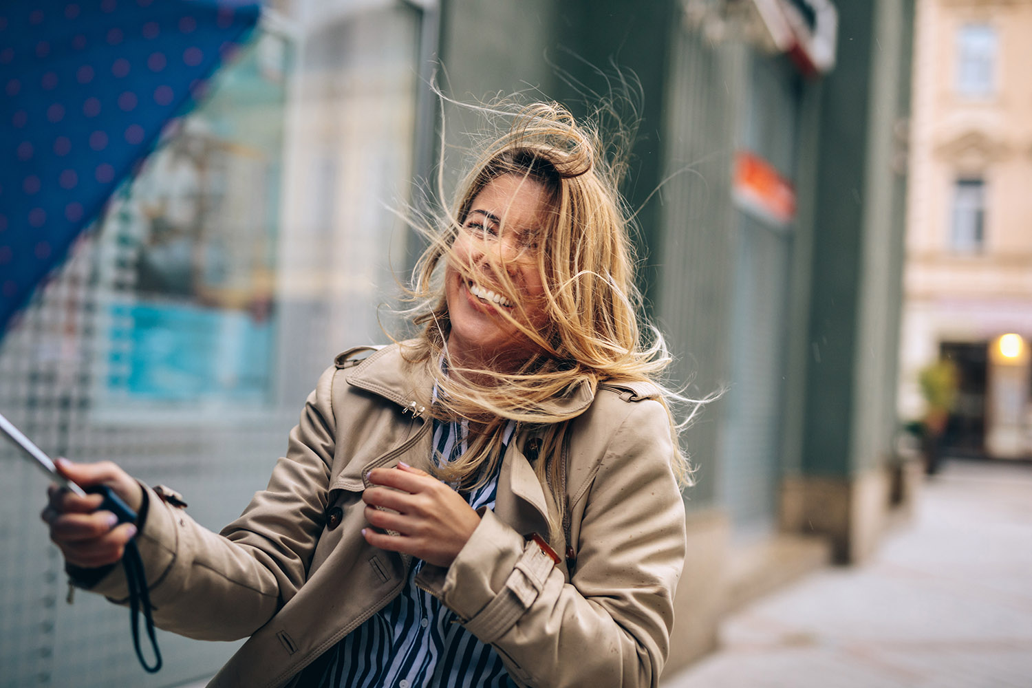 Frau lachend im Wind mit Schirm in der Hand