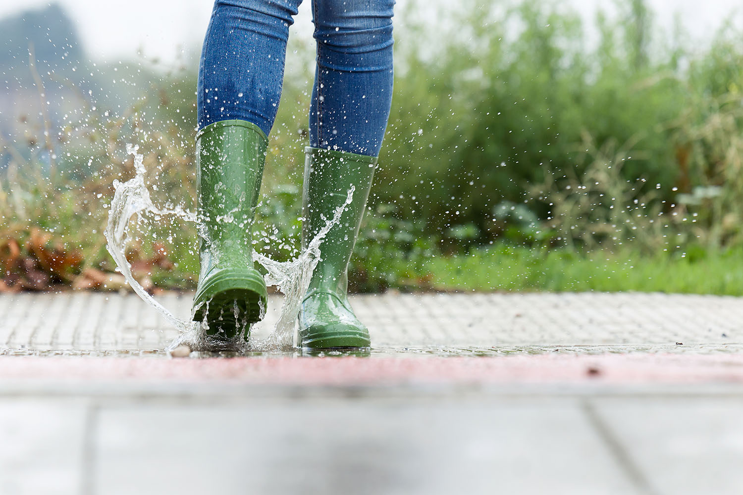 Person mit grünen Gummistiefeln springt in Pfütze.