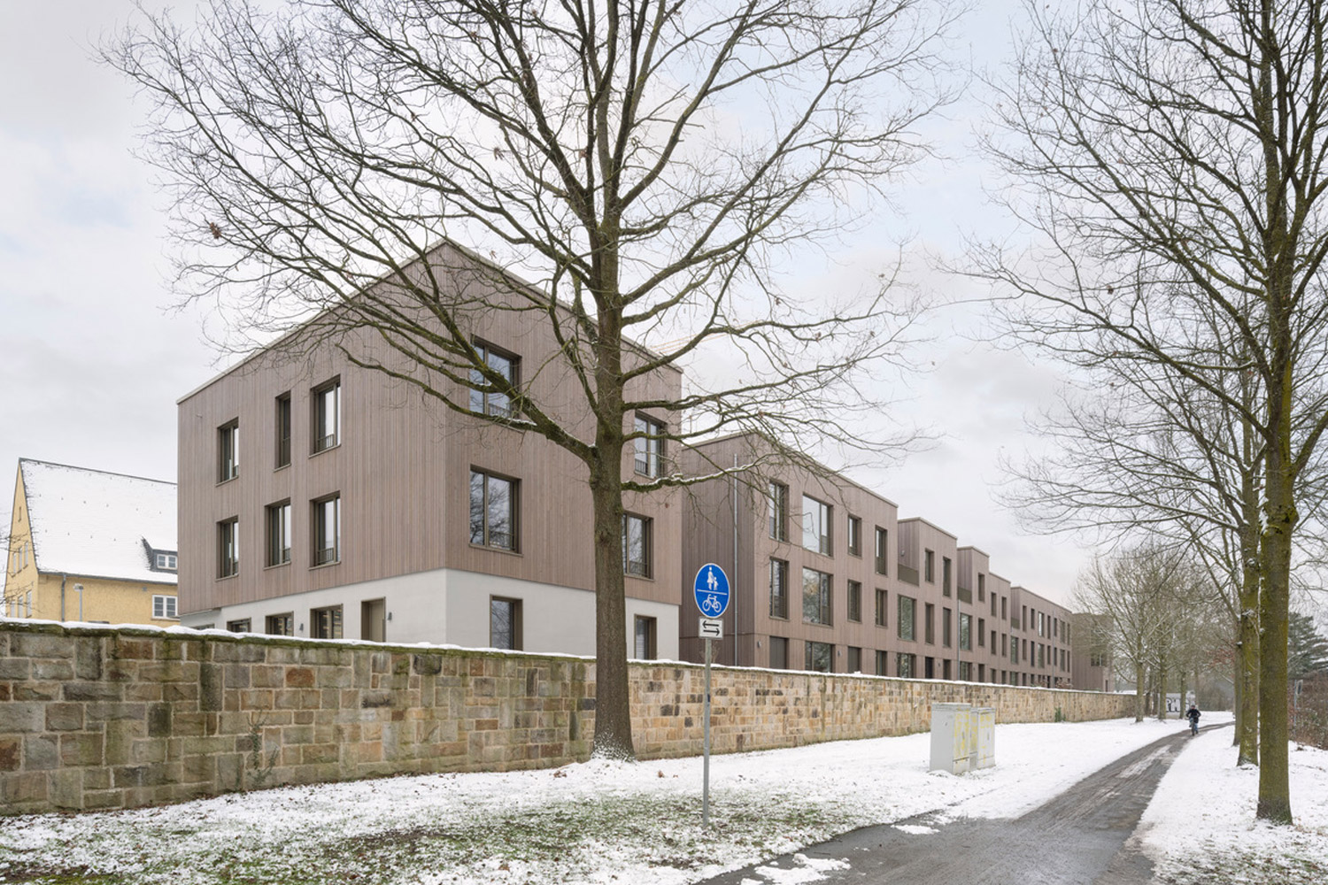 Holzgebäude hinter einer Sandsteinmauer