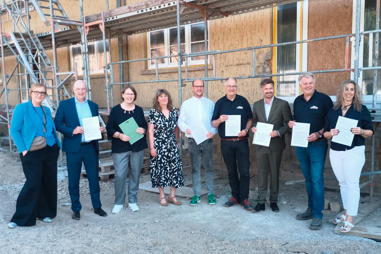 Gruppenfoto mit neun Personen vor einer Baustelle, die Urkunden in den Händen halten