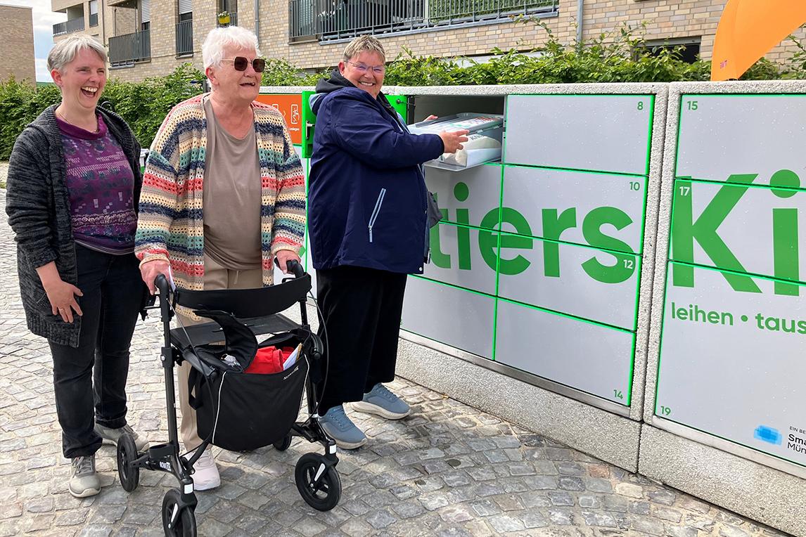 Drei Frauen neben einer Ausleihstation mit der Aufschrift „Quartierskiste“