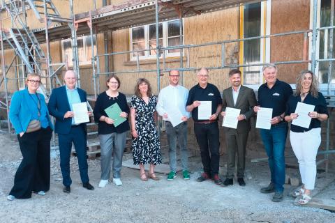 Gruppenfoto mit neun Personen vor einer Baustelle, die Urkunden in den Händen halten